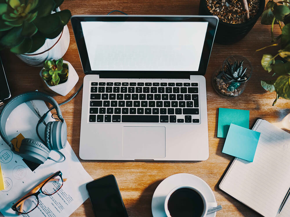 Laptop, Mobile, Glasses, Coffee Cup, Notepad on Table for Remote Work.